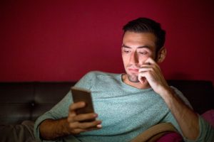 thoughtful-man-using-smartphone-sofa-night